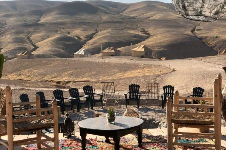 Photo by Chai Carabuena Serene desert camp view with wooden chairs and Moroccan landscape.